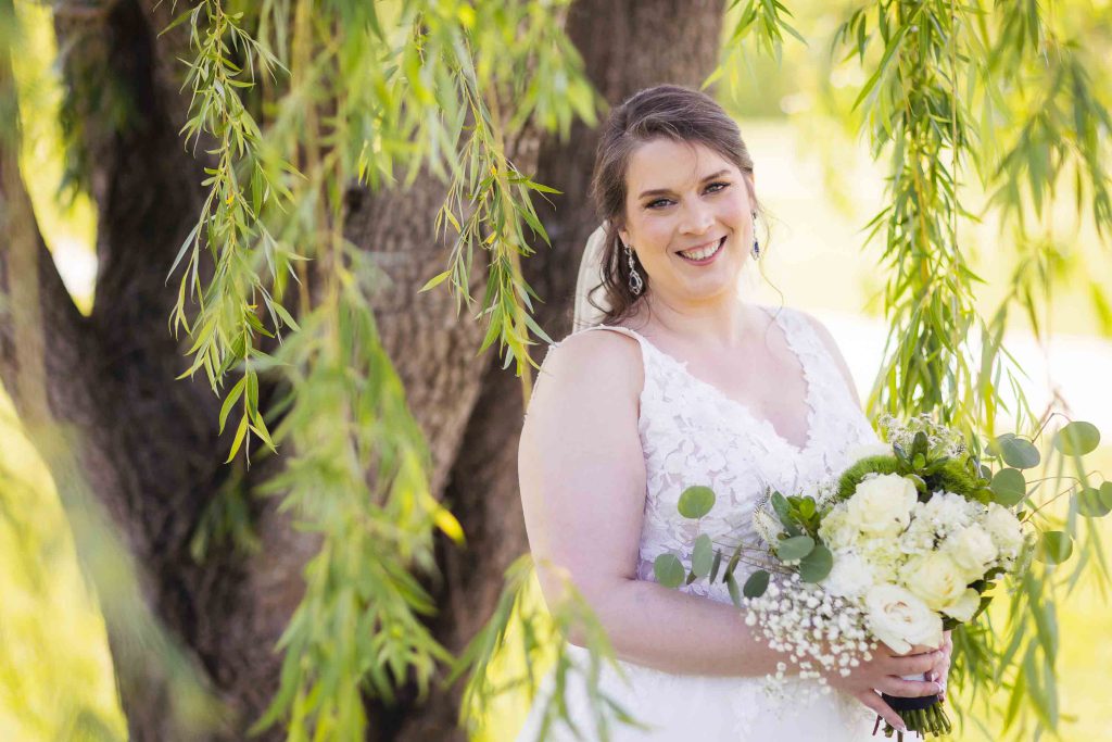 A bride is standing under a willow tree for her wedding portrait.