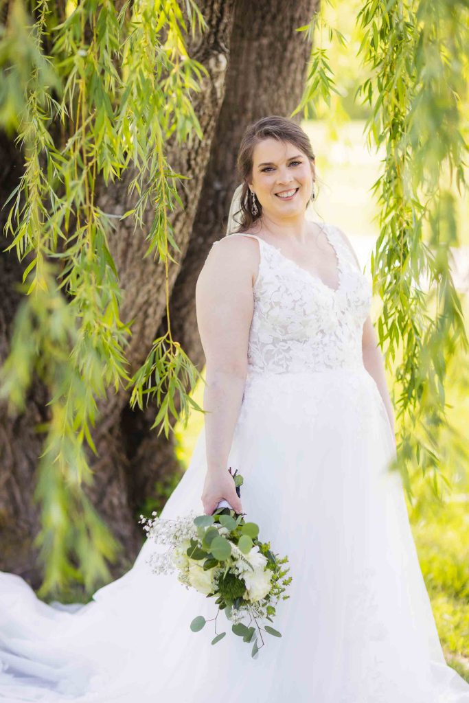 A bride in a wedding dress posing for a portrait under a willow tree.