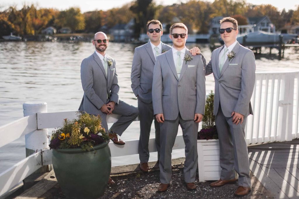 A group of groomsmen posing for a wedding portrait on a dock.