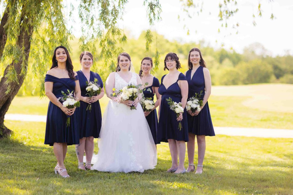A wedding portrait featuring bridesmaids posing in front of a willow tree.