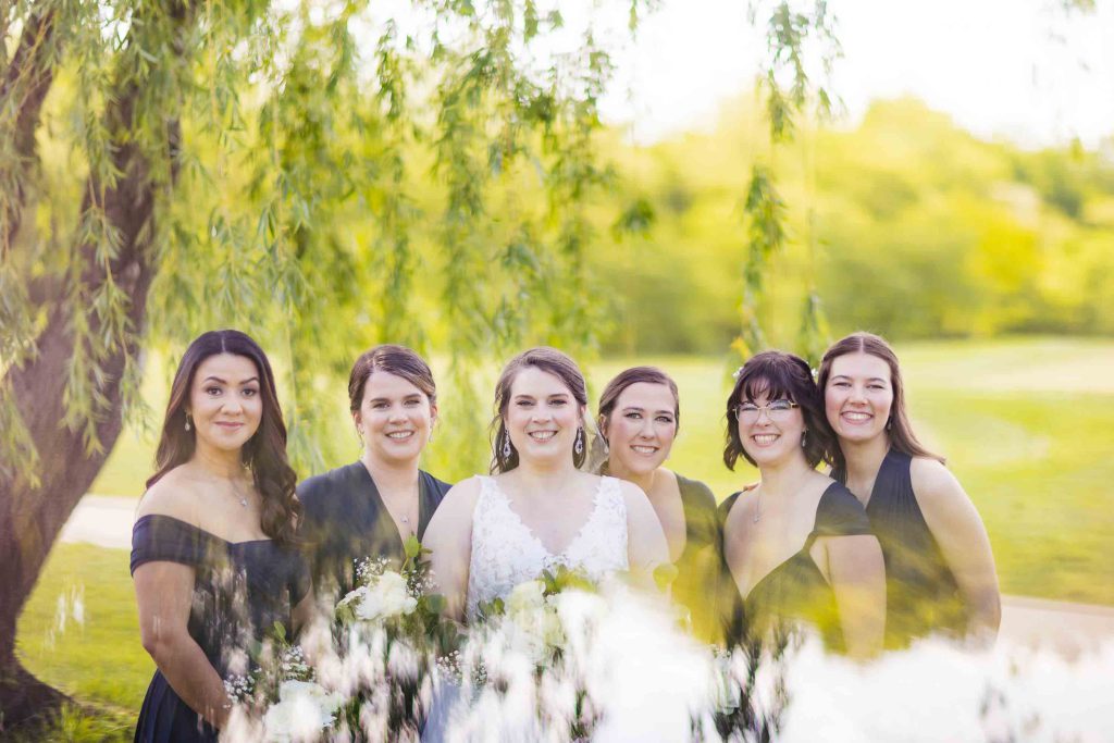Bridesmaids posing for a wedding portrait in front of a willow tree.