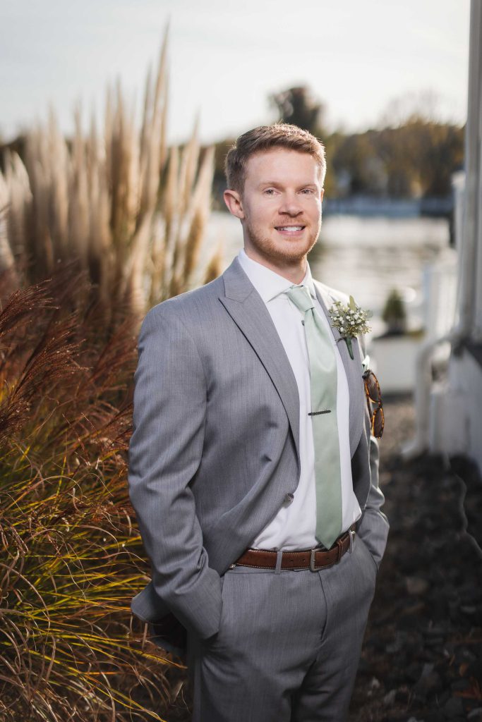 A groom in a wedding suit standing by a body of water.