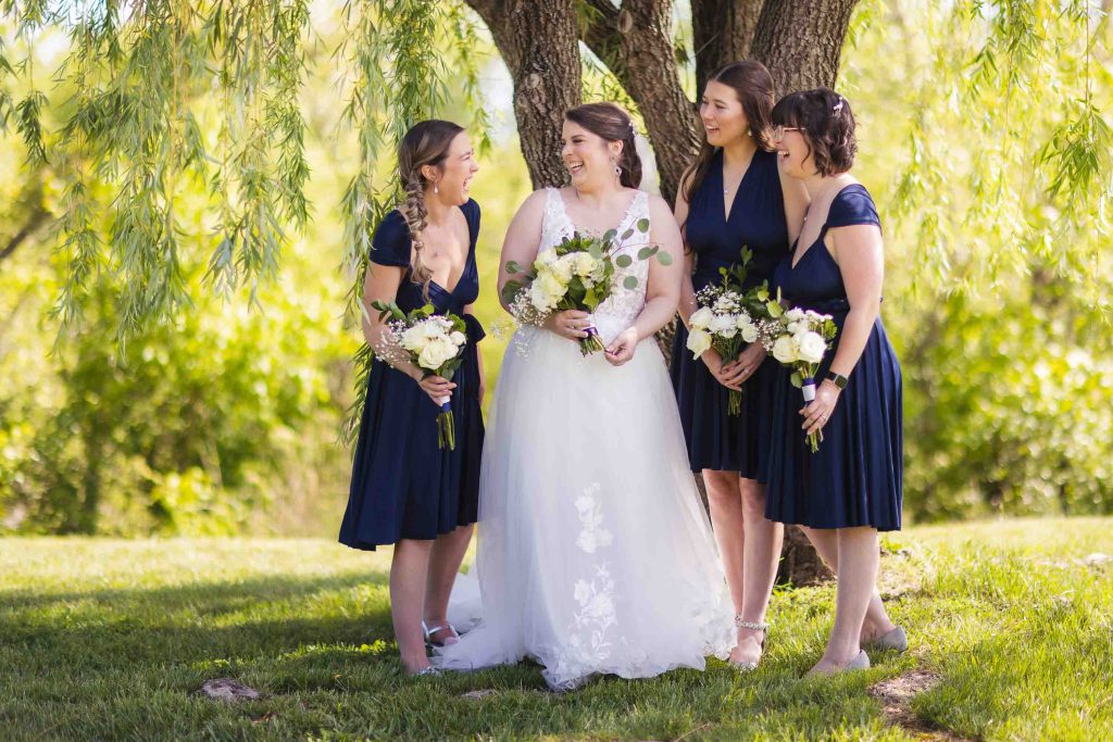 The bride and her bridesmaids are posing for a wedding portrait under a tree.
