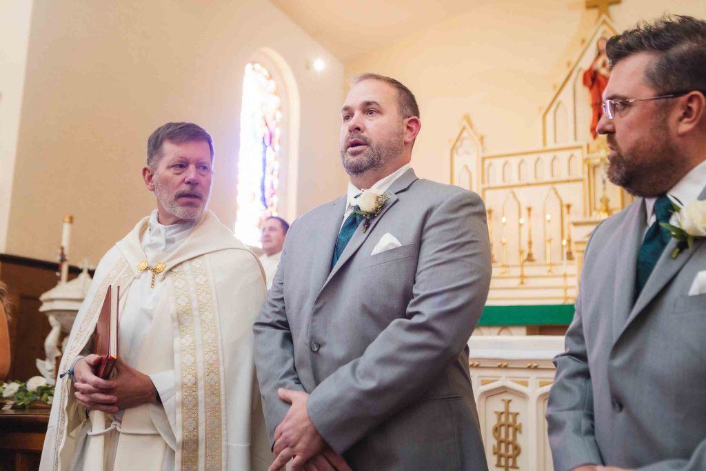 Groom and groomsmen participating in a wedding ceremony with a priest.
