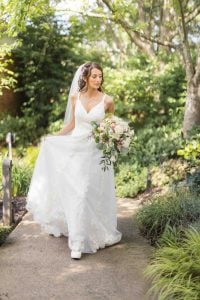 A bride in a white wedding dress walks down a woodland path.