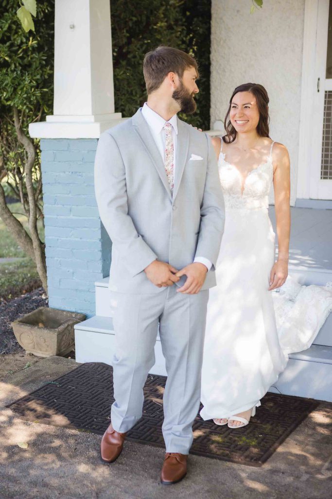 A candid wedding preparation moment captured as the bride and groom stand on the steps of a house.