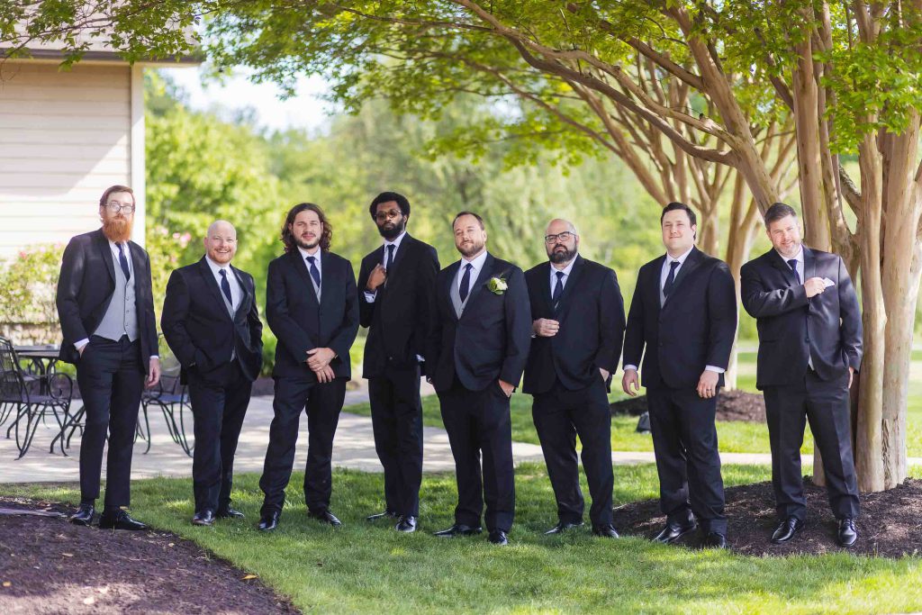 A group of groomsmen posing in front of a tree at a wedding.