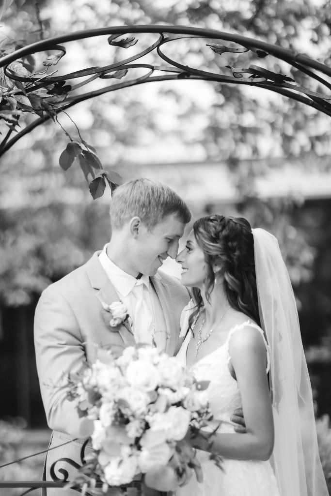 A black and white portrait of a bride and groom at their wedding ceremony in front of an arch.