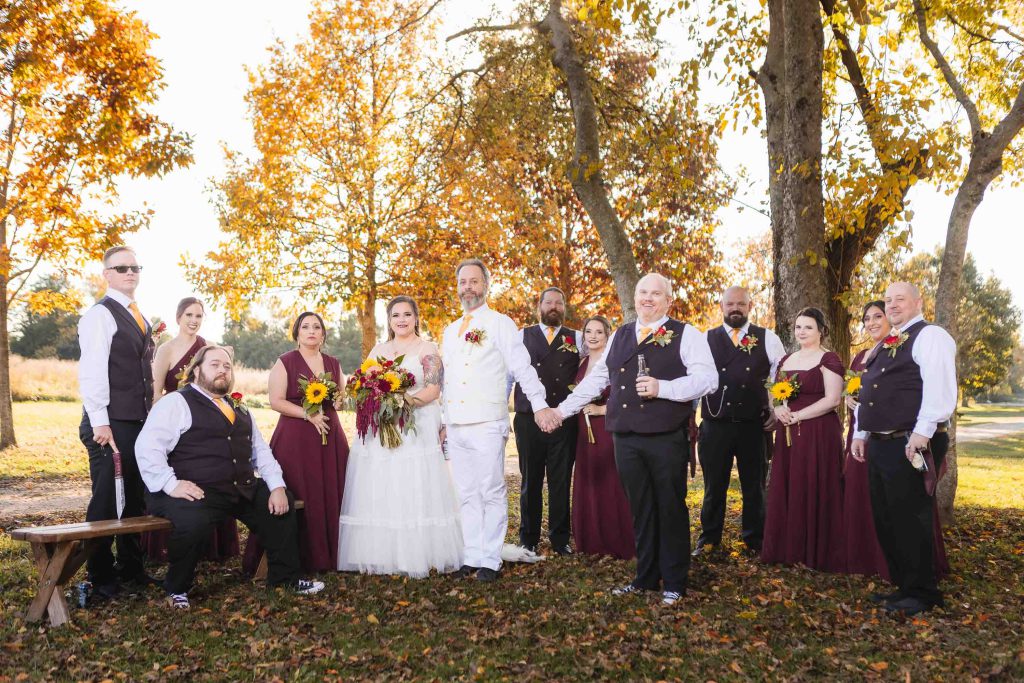 A group of bridesmaids and groomsmen posing for a wedding portrait in the fall.