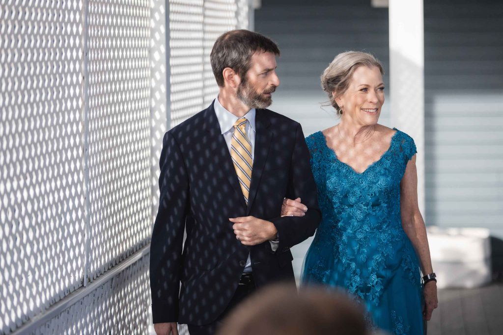 A man and woman in a blue dress walking down a walkway during a wedding ceremony.