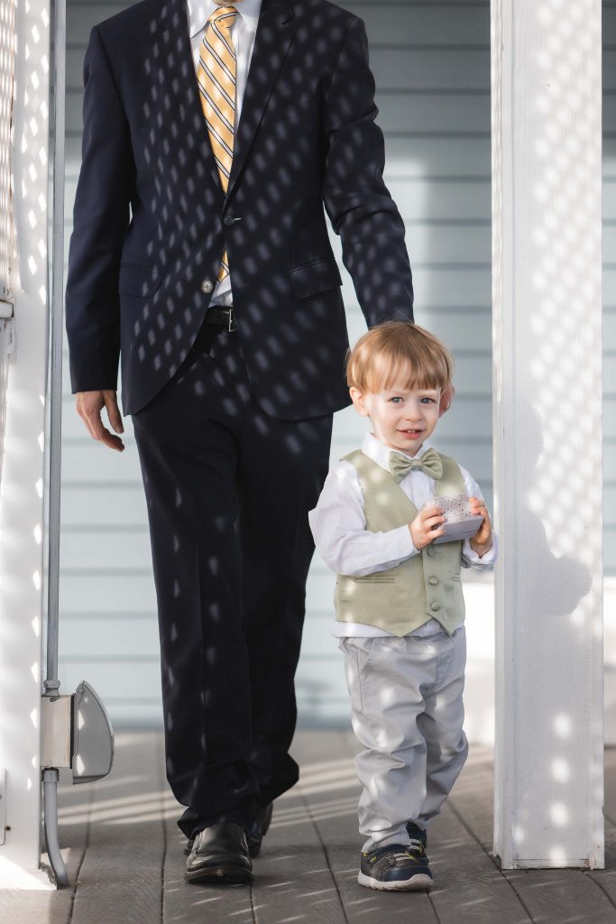 A man in a suit walking with a little boy at a wedding ceremony.