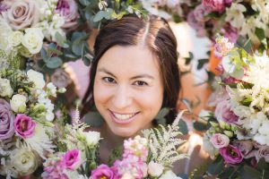 A woman smiles in front of a bunch of flowers for her wedding portrait.