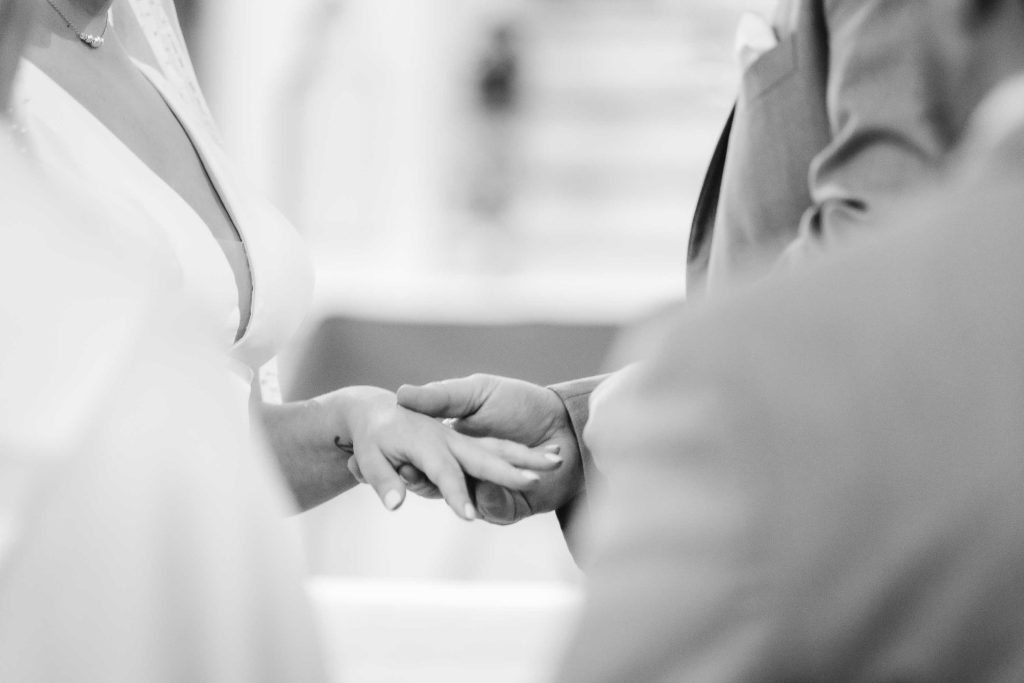 A bride and groom during their wedding ceremony, holding hands.
