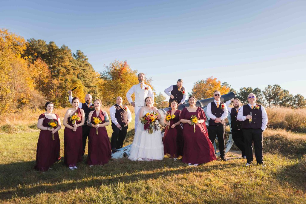 A group of bridesmaids and groomsmen posing in a field for a wedding portrait.