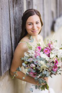 A wedding portrait with a bride holding a bouquet in front of a wooden wall.