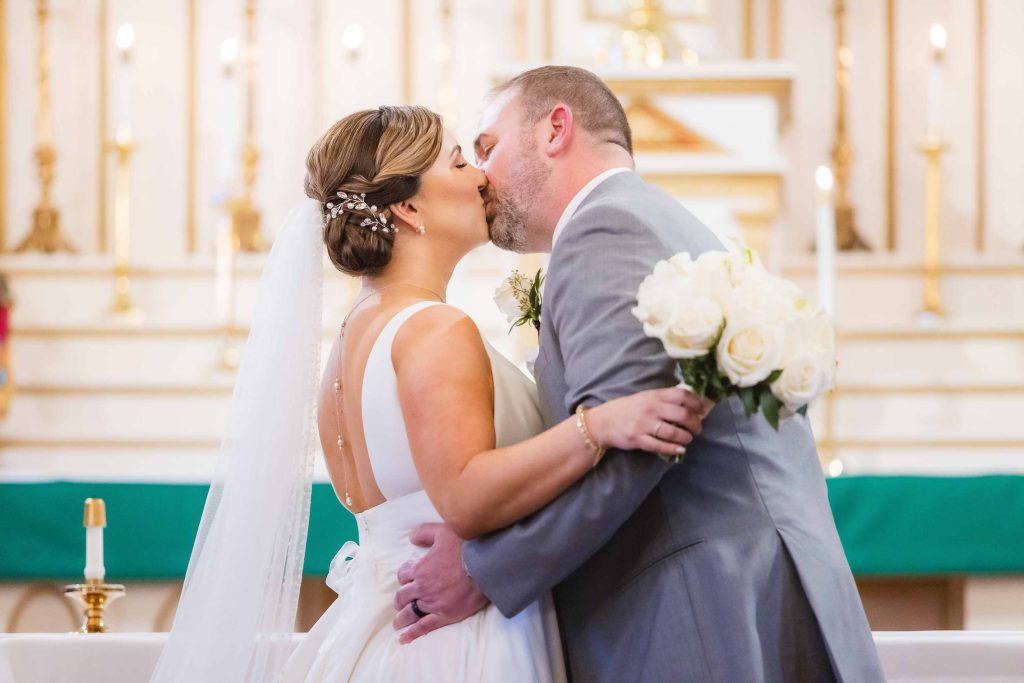 A couple exchanging a ceremonial kiss outside of a church during their wedding.