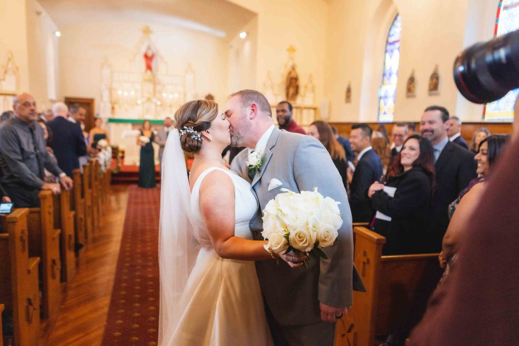 A bride and groom kissing at their wedding ceremony in a church.