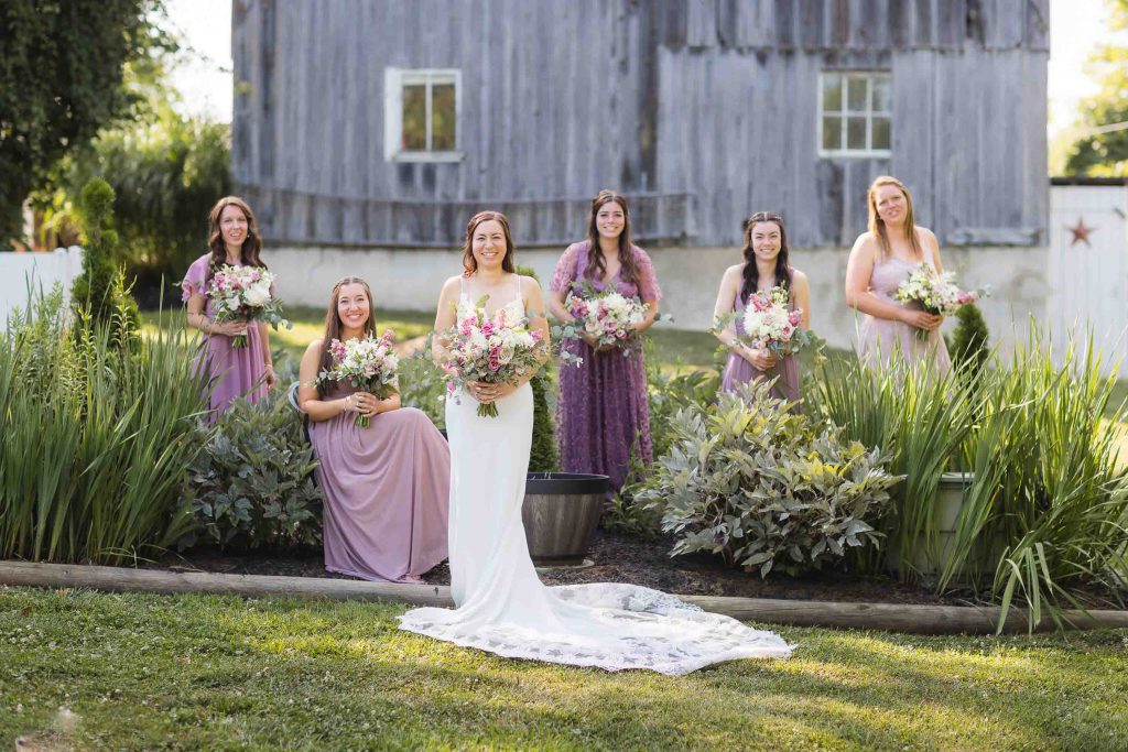 A wedding party poses in front of a barn for a portrait.