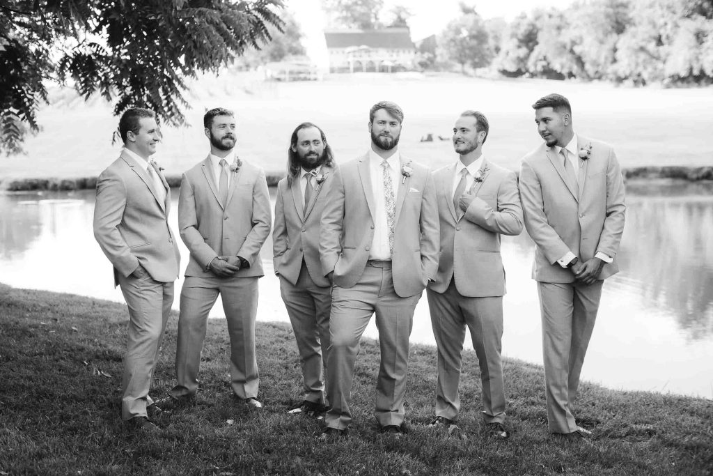 A group of groomsmen posing for a wedding portrait next to a pond.