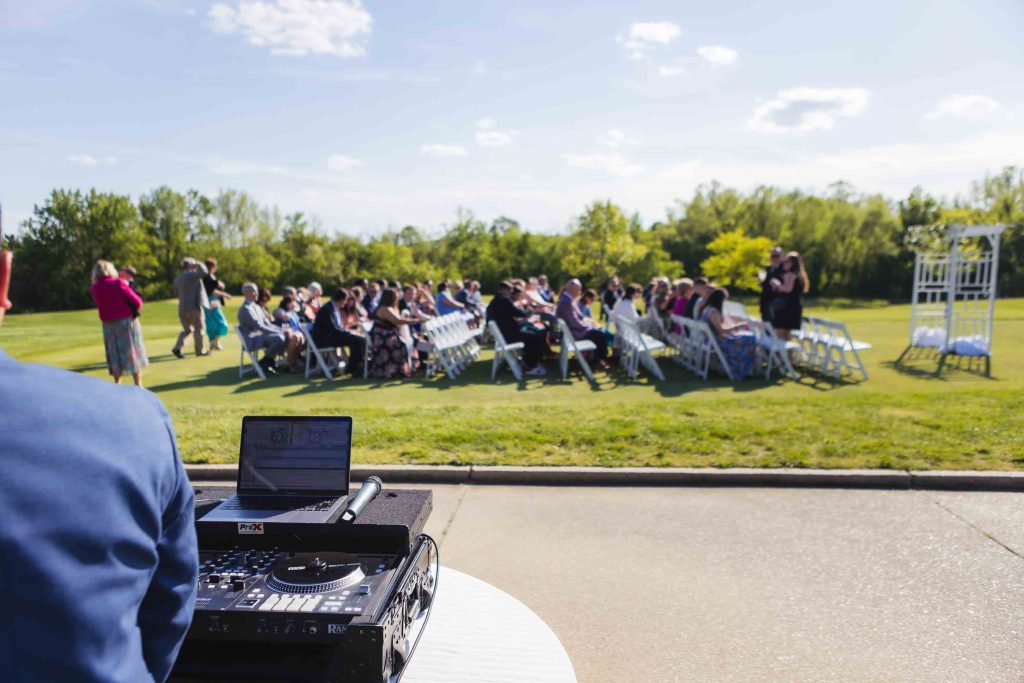 A man is playing a DJ at an outdoor wedding ceremony.
