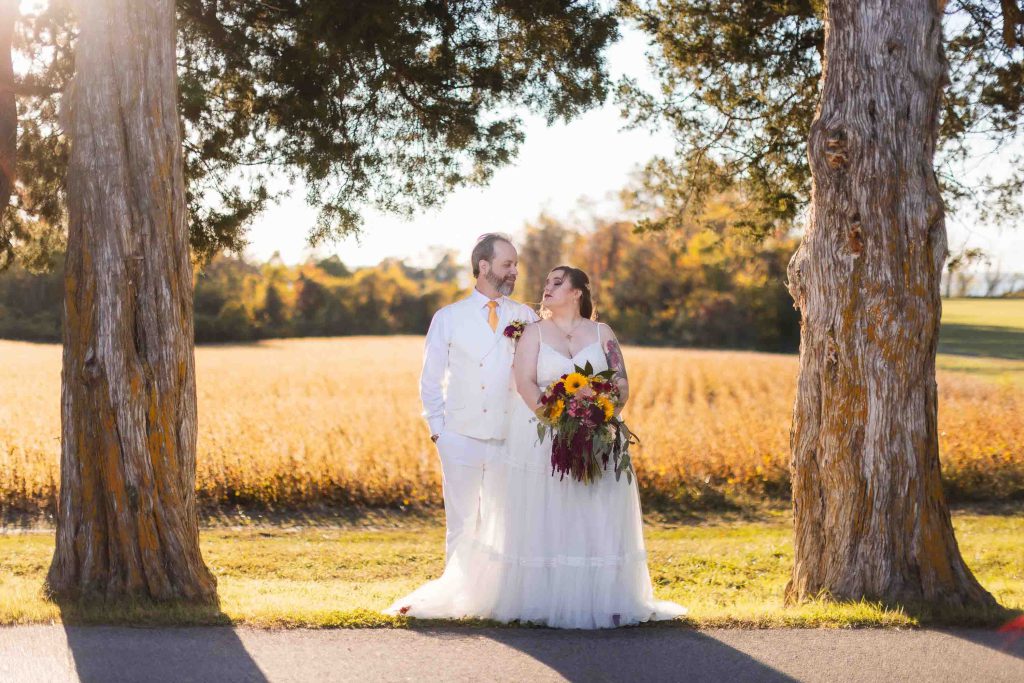 A wedding portrait of a bride and groom standing next to trees in a field.