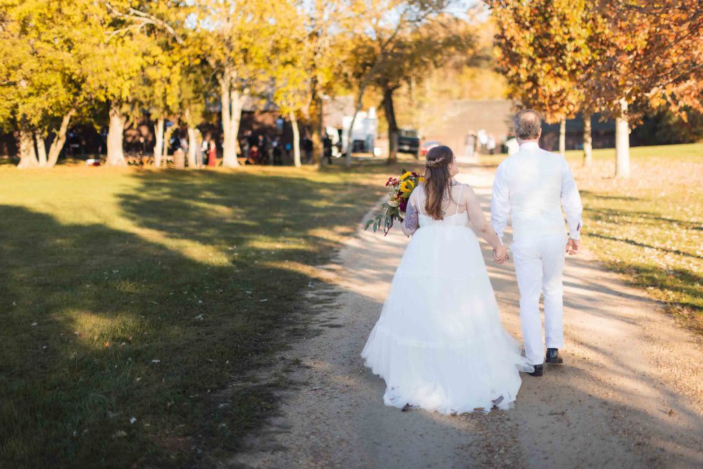 A wedding portrait of a bride and groom walking down a dirt path.