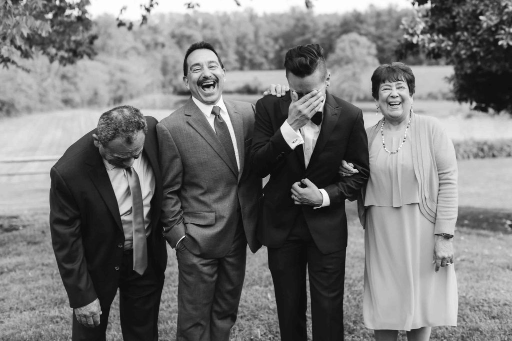 A black and white wedding portrait of a group of people laughing.