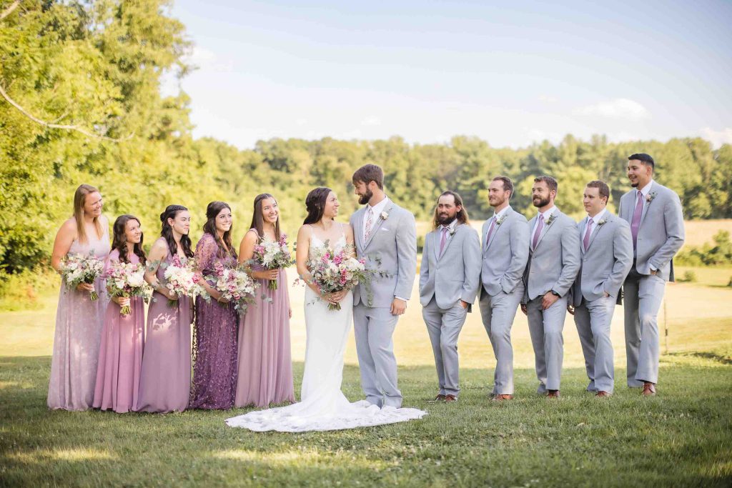 A group of bridesmaids and groomsmen posing for a wedding portrait in a field.