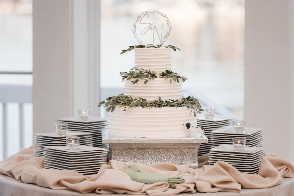 A detailed white wedding cake with greenery on top.
