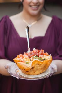 A woman holding a bowl of tacos at a wedding.