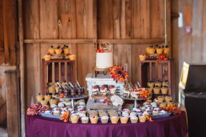 A wedding dessert table with a variety of desserts displayed in a barn.