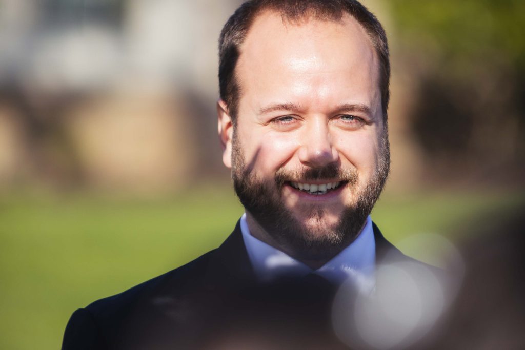 A man in a suit and tie is smiling at a wedding ceremony.