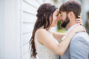 A bride and groom embracing in front of a white house for their wedding portrait.