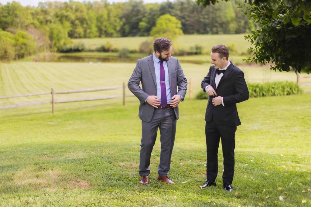 Two men in tuxedos standing in a field for a portrait.