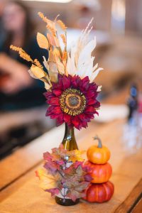 A sunflower in a wine bottle sits on top of a wooden table, adding details to a wedding decor.