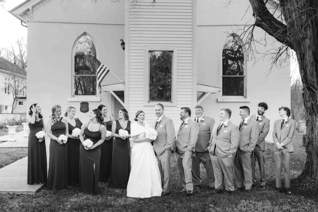 A black and white portrait of a wedding party in front of a church.