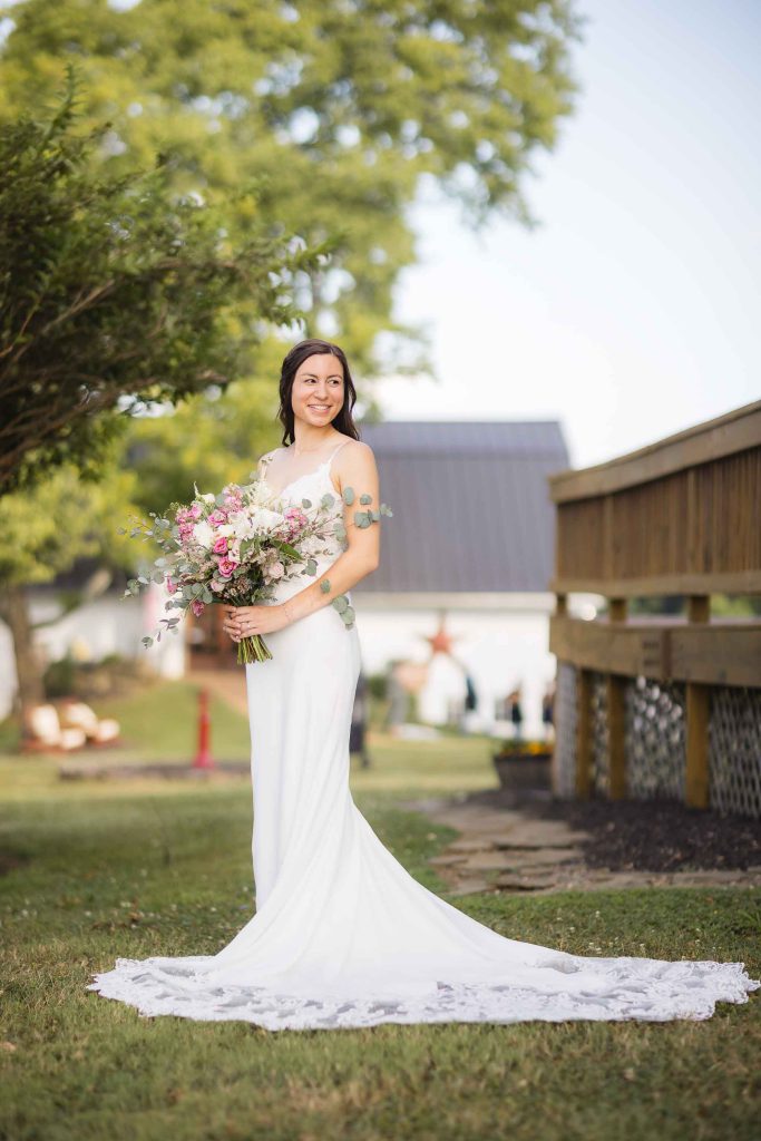 A wedding portrait of a bride holding her bouquet in front of a barn.