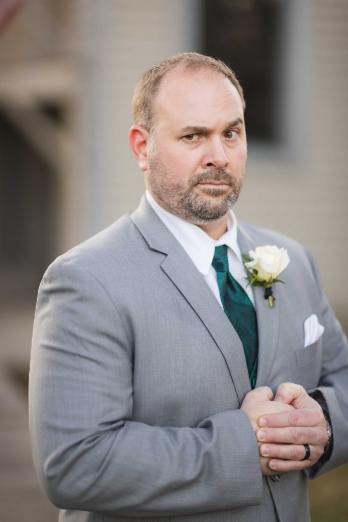 A man in a suit and tie standing in front of a house for a wedding portrait.