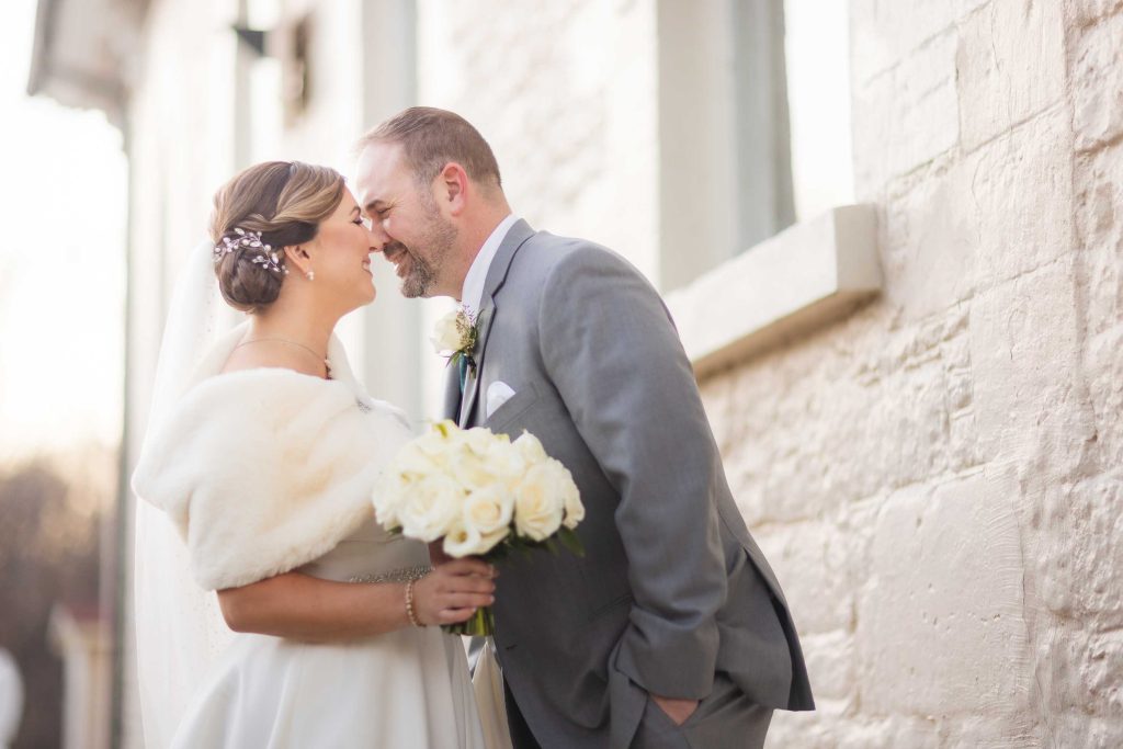 A bride and groom kissing during their wedding portrait session in front of a stone wall.