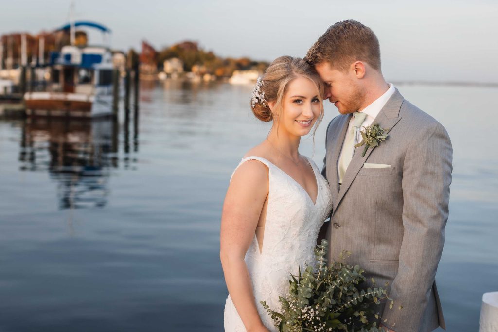 A wedding portrait of a bride and groom standing on a dock.