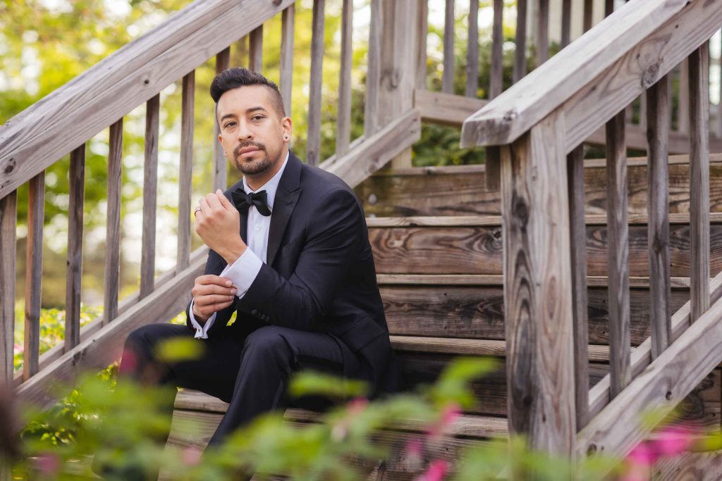 A man in a tuxedo sitting on a set of stairs for a wedding portrait.