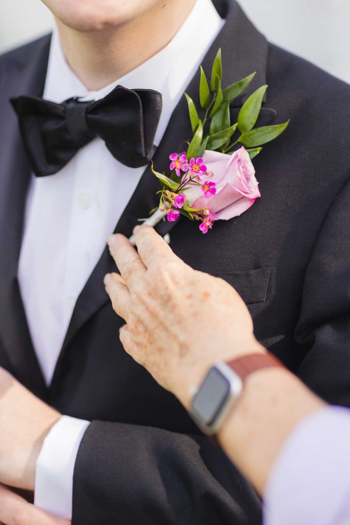 A man in a tuxedo is adjusting his boutonniere for a wedding.
