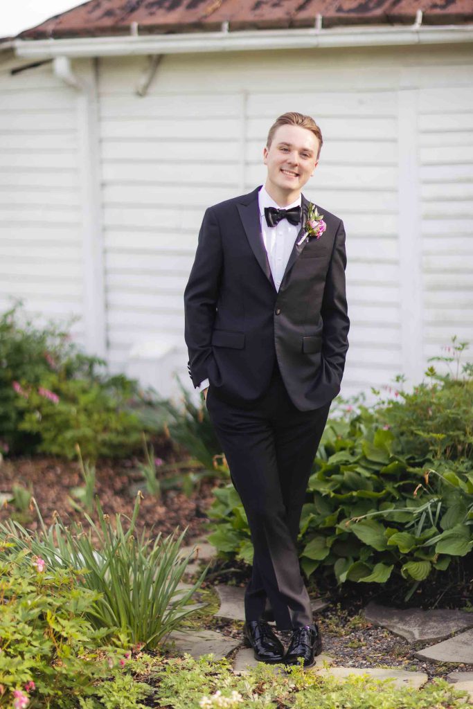 A groom in a tuxedo standing in front of a house for his wedding portrait.