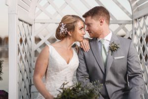 A wedding couple embracing in front of a gazebo.