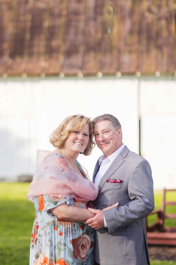 An older couple posing for a wedding portrait in front of a barn.
