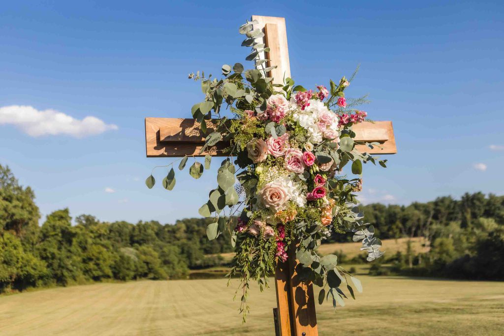 A wooden cross adorned with flowers and greenery in a field.