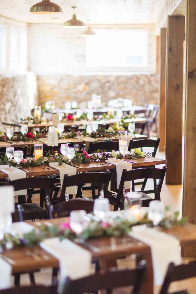 A rustic wedding reception with wooden tables and greenery - showcasing intricate details.