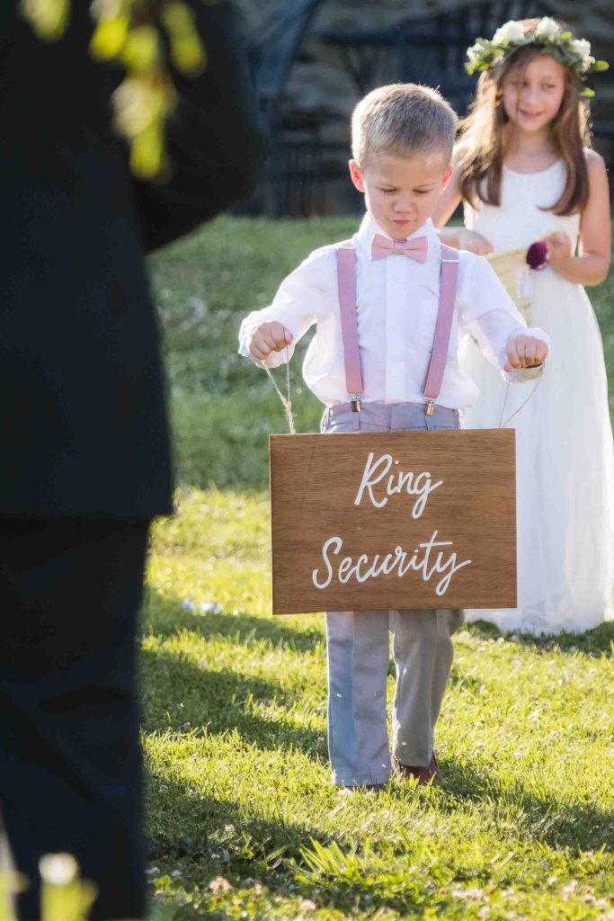A little boy participating in a wedding ceremony, holding a sign that says ring security.
