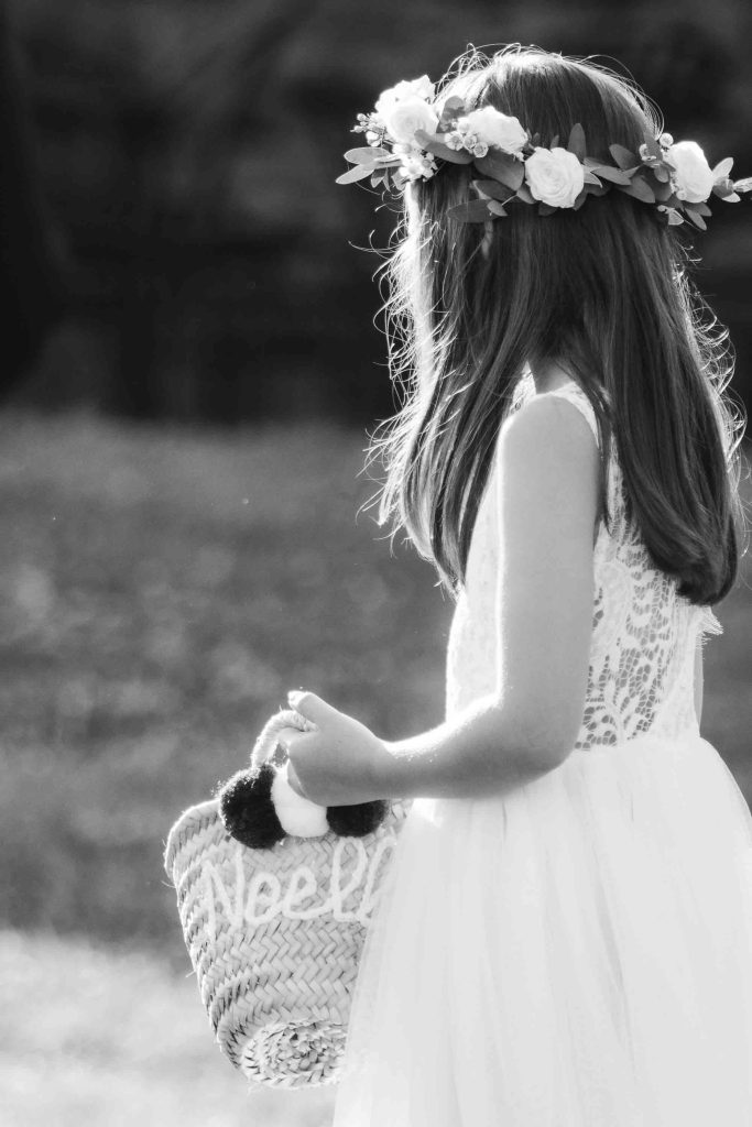 A little girl in a flower crown participating in a wedding ceremony, holding a basket.