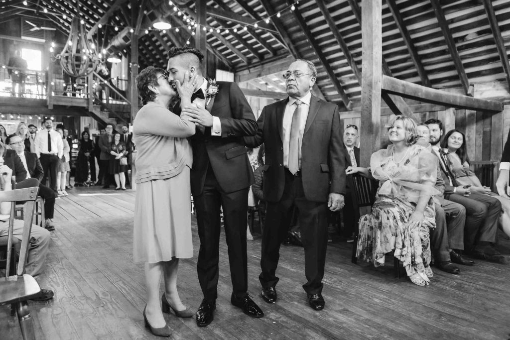 A bride and groom kiss during their rustic wedding ceremony in a barn.